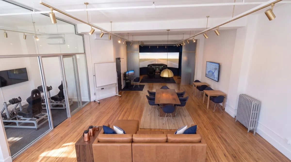 AI-generated rendering of the Aviator.NYC training studio in Midtown Manhattan seen from above: conference and lounge area by the street windows, two VR simulators in the glass room, briefing tables, and the Cirrus G3000 simulator bay at the back